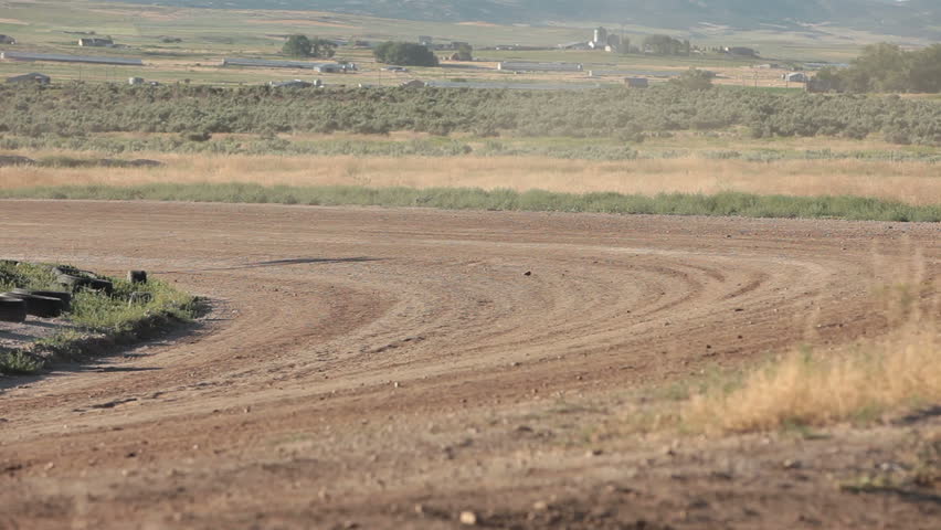 Race stock cars on dirt oval course. Highly modified stock cars driving and racing on a very dirty and dusty track corner. Warmup lap testing the road and track conditions.