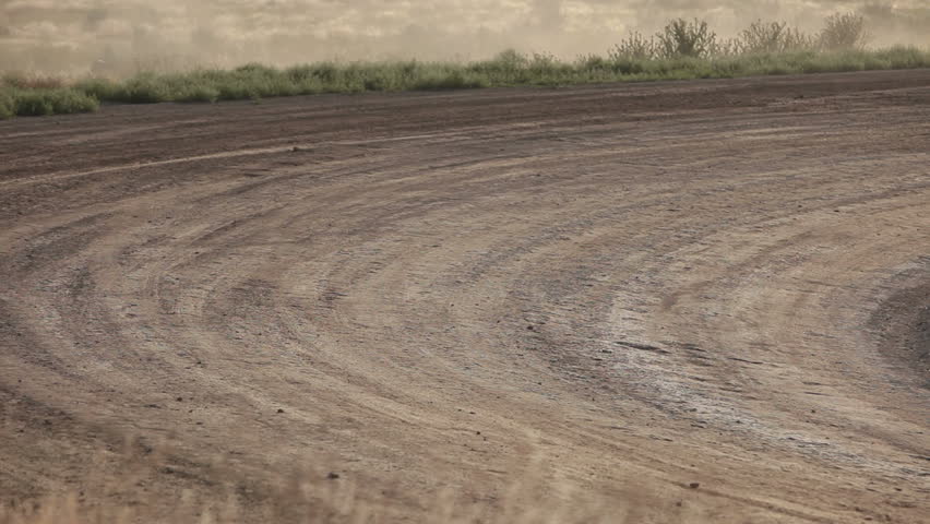 Race cars speed on dirt oval course. Highly modified stock cars driving and racing on a very dirty and dusty track corner. High speed around dusty corner towards view.
