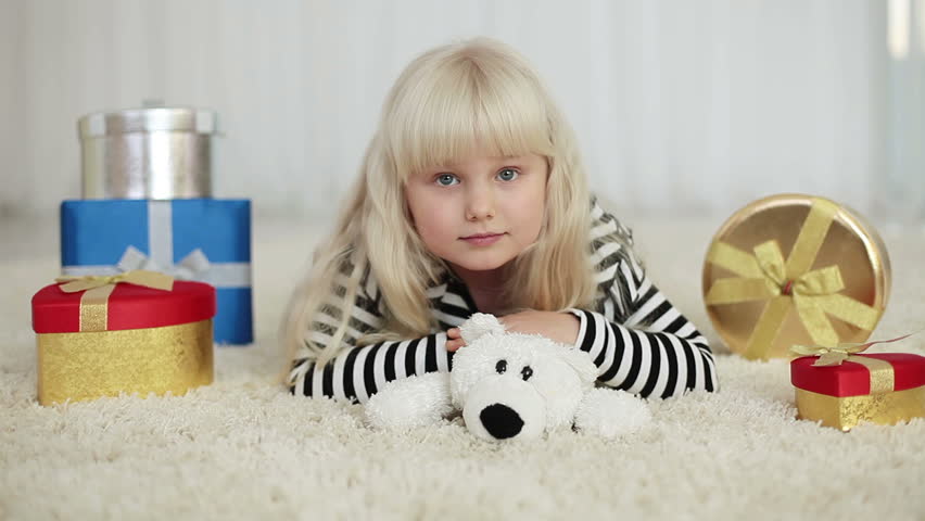 Happy girl with a teddy bear lying beside gifts 