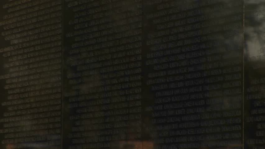 WASHINGTON, D.C. - CIRCA 2009: View moves upward from small flags edging the Vietnam War Memorial Wall, to a larger flag reflected over names on the wall.