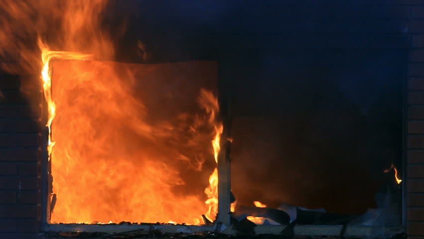 Fire burning at night, intense house burning with flames and smoke coming through broken window.