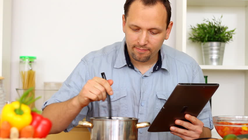 Man in kitchen looking at recipe on electronic tab during cooking
