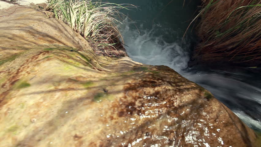 Dolly over the top of a waterfall at the Ein Gedi Nature Reserve in Israel, showing the water splashing into the pool at the bottom of the waterfall.
