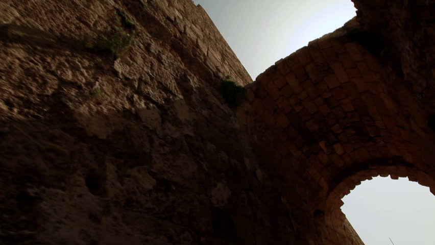 Slider dolly move under an archway, low angle looking up at the arch.  At the end of the move the sun is revealed shinning over these ruins at Caesarea in Israel.