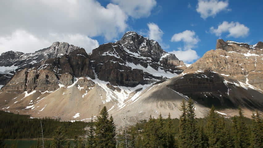 Mountain peaks and glaciers under beautiful fluffy clouds and deep blue sky. Clouds floating past drawing shadows and textures across hills and lake. Banff National park, Canada. Rocky Mountains.