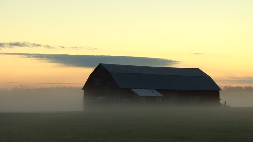 Red barn engulfed in mist during sunrise