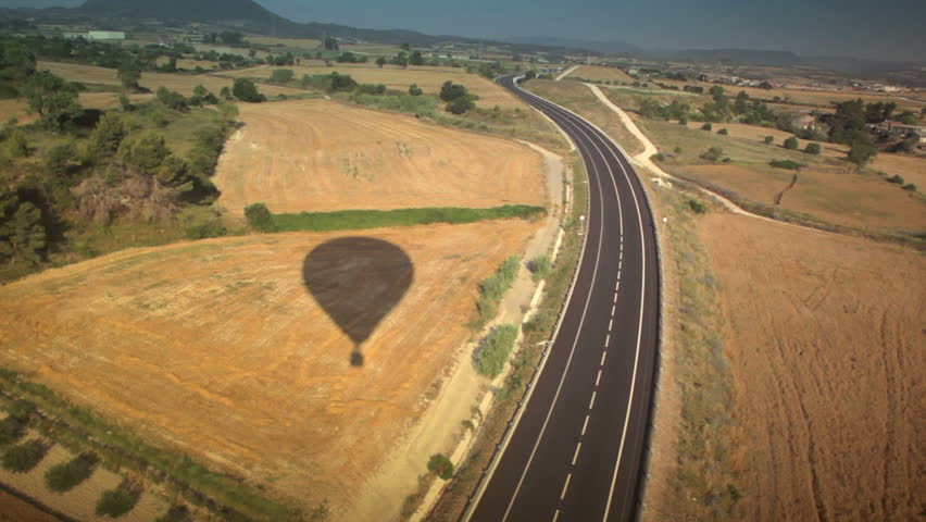 wide aerial shot with balloon shadow and vehicle passing with corn fields 