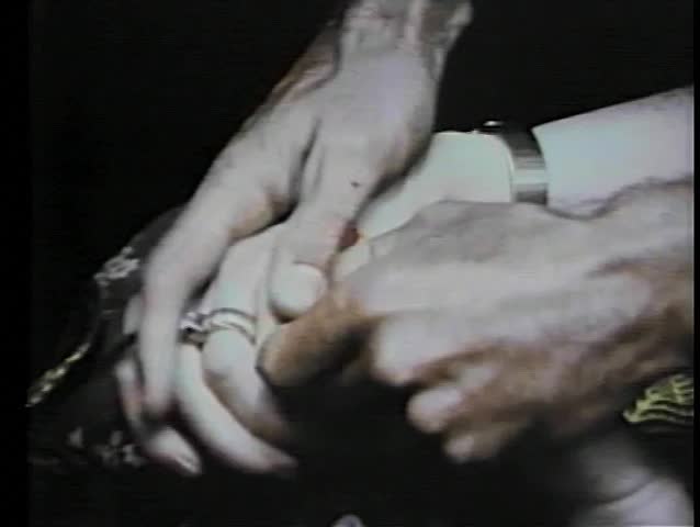 Close-up hands removing African pendant from dead woman's grasp