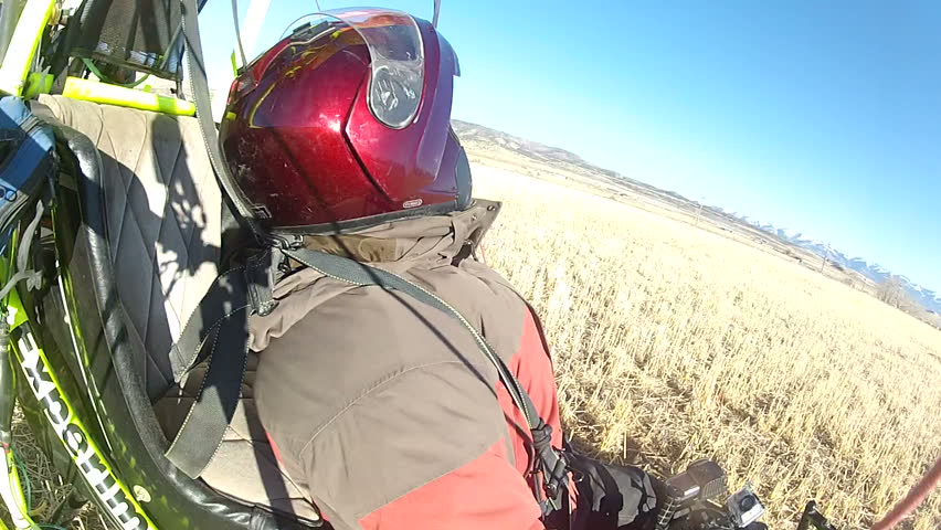 Pilot in an ultralight powered parachute aircraft lands in rural farm land. Winter cold temperature wearing helmet and coat and gloves. Recreation and exciting way to travel.