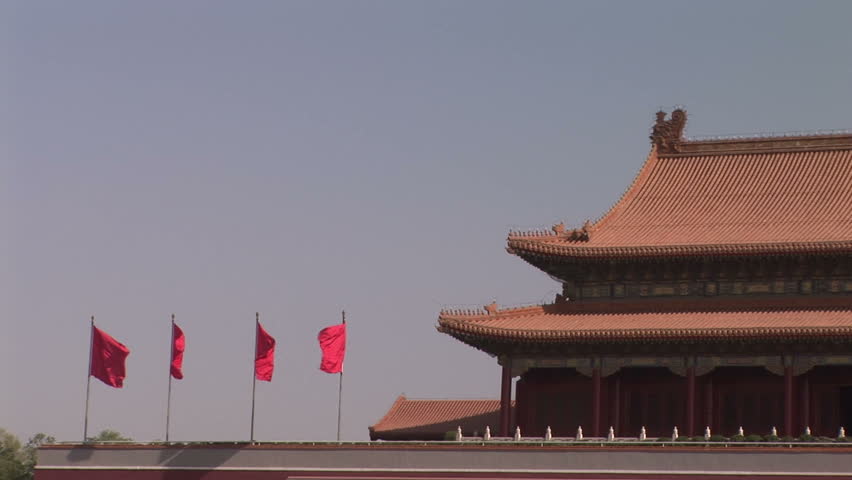 Four red flags flapping in the wind against a grey sky over the Forbidden City in Beijing, China