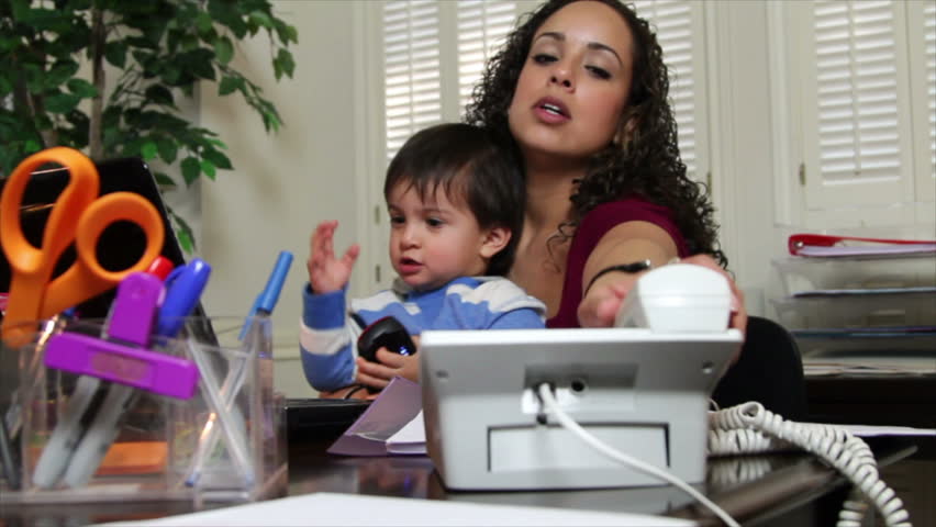 A pretty Hispanic mom in her home office trying to get her work done while her little son sits in her lap.