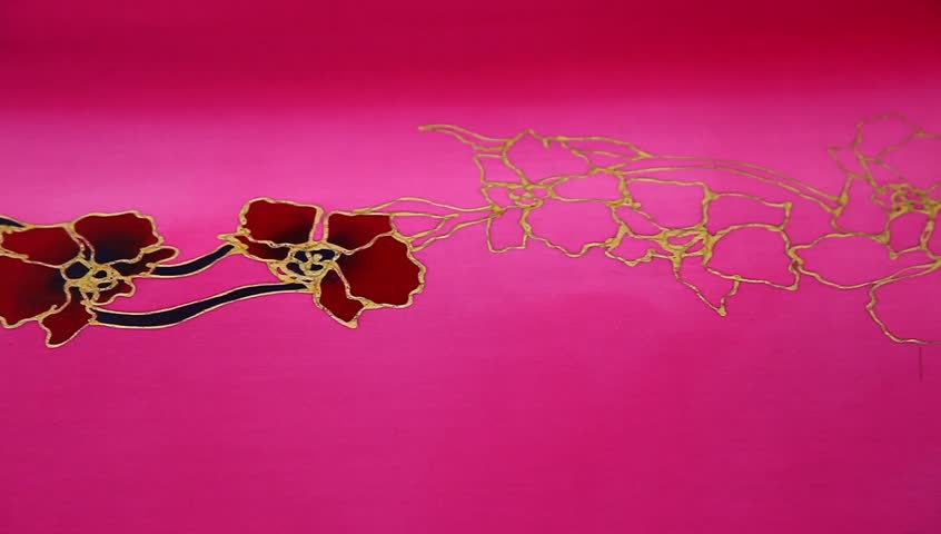 An artist carefully paint the flower motif on a pink batik fabric 