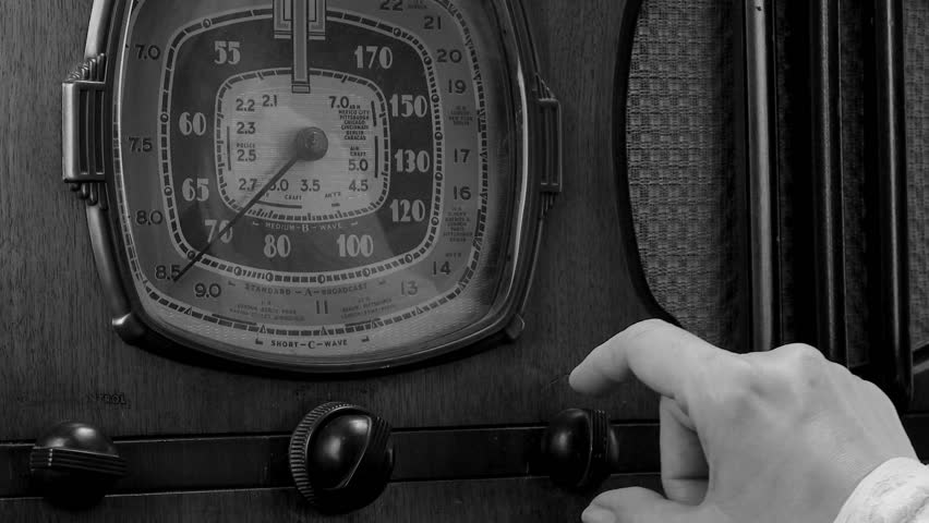 Female hand turning on and tuning a antique radio, black and white