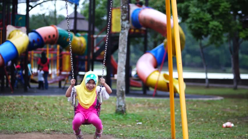 Young Muslim girl wearing scarf play swing happily at playground