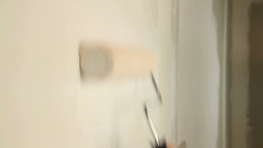 Painting out a bare wall with a paint roller with white paint.