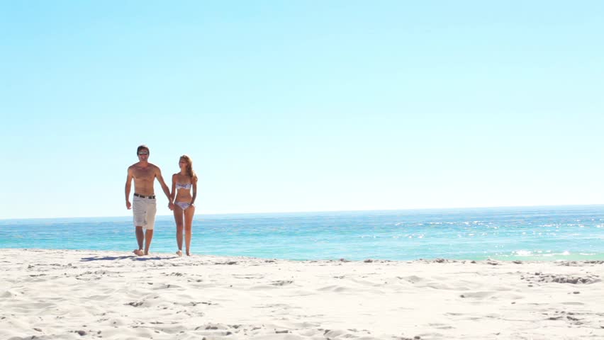 Romantic couple on honeymoon walk along a pristine beach in summer. gorgeous blue ocean and clear sky.