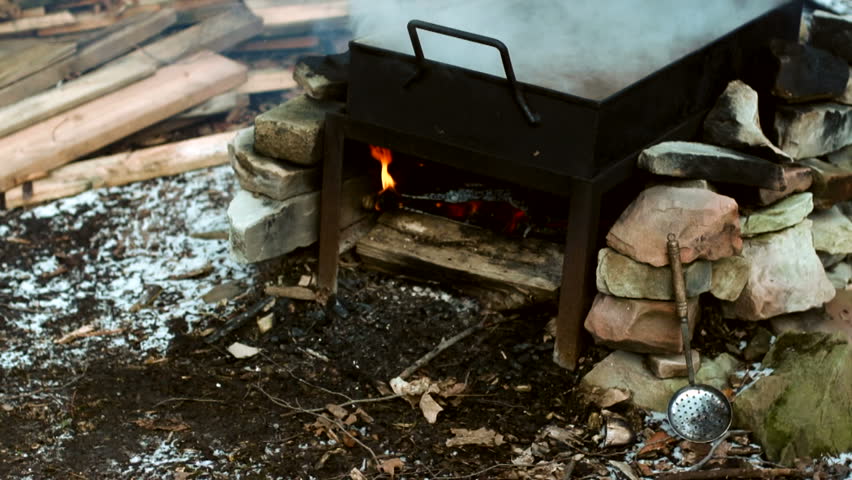 Wood fire under a Evaporation Pan filled with maple sap during the annual maple syrup making time in the sugar-bush. A traditional way of making maple syrup.