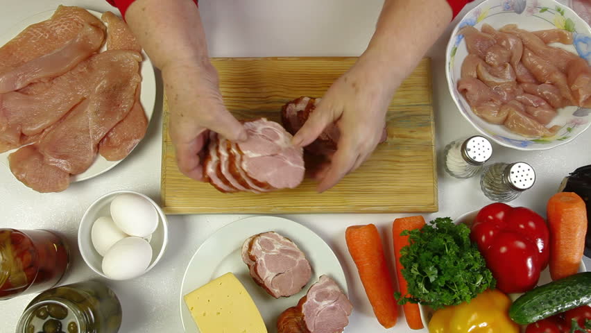 Women's hands slicing pork bacon, an ingredient for cooking chicken roll. Top view