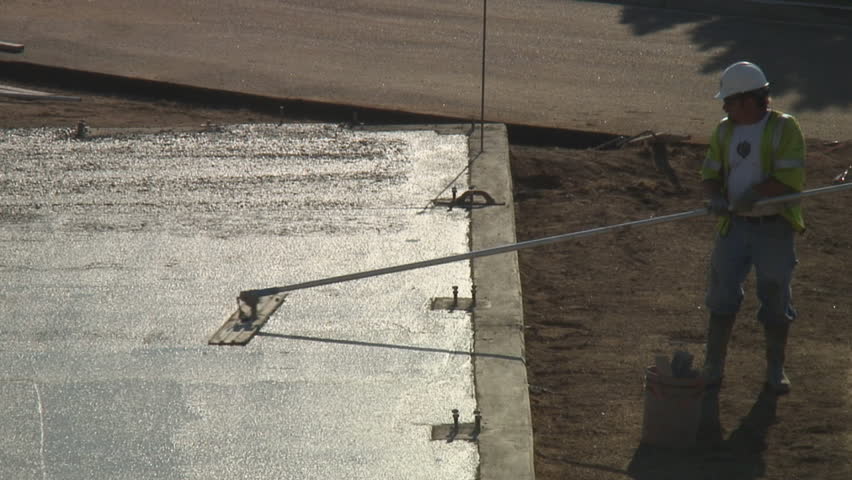 Construction worker finishes pouring concrete floor by troweling the cement in early morning