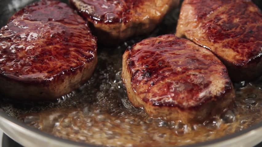 Beef steaks being fried and poured with butter