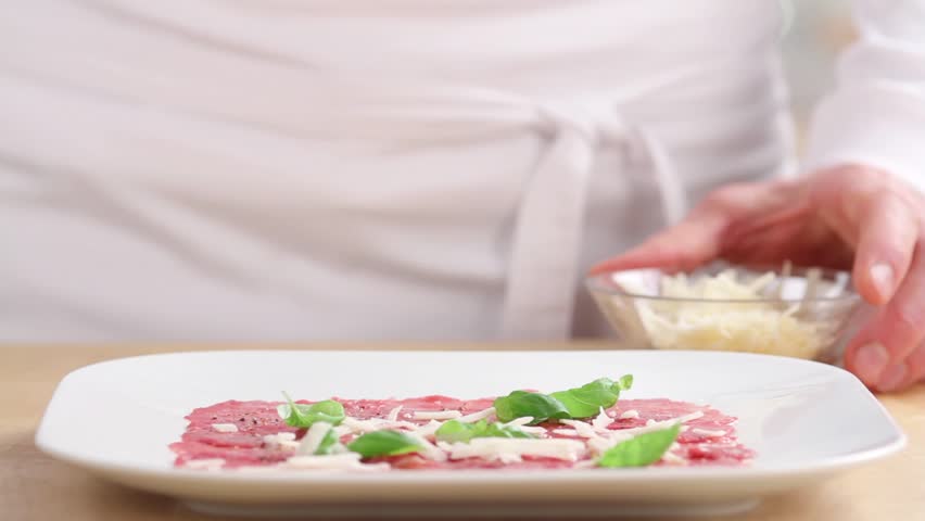 Beef carpaccio being sprinkled with freshly grated parmesan