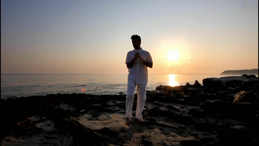Handsome man practicing thai chi on the beach at sunrise