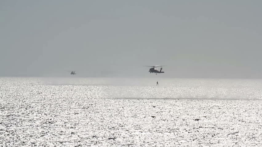 Search and Rescue training. A group of two helicopters flying low above the water. One of them is recovering person from water
