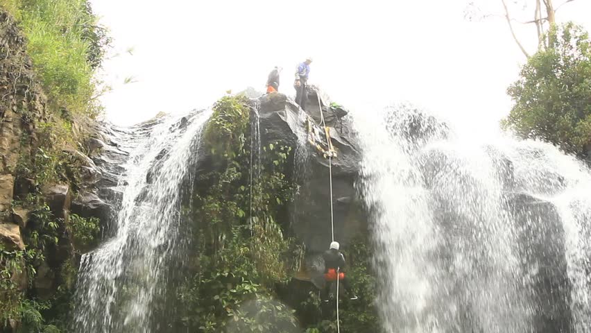 footage of a pesrson rappelling a waterfall.locked down, wide angle shot in Ecuadorian rainforest.