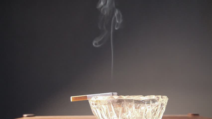 Smoke of a cigarette on ashtray isolated on grey background. Close up. Studio shot.