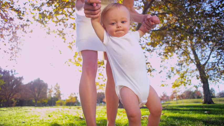 Cute baby being supported by the mother while the baby takes the first steps outdoors