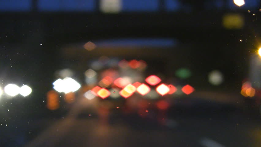 Defocused lights. Rainy highway drive. Emergency lights pass by and traffic slows.
