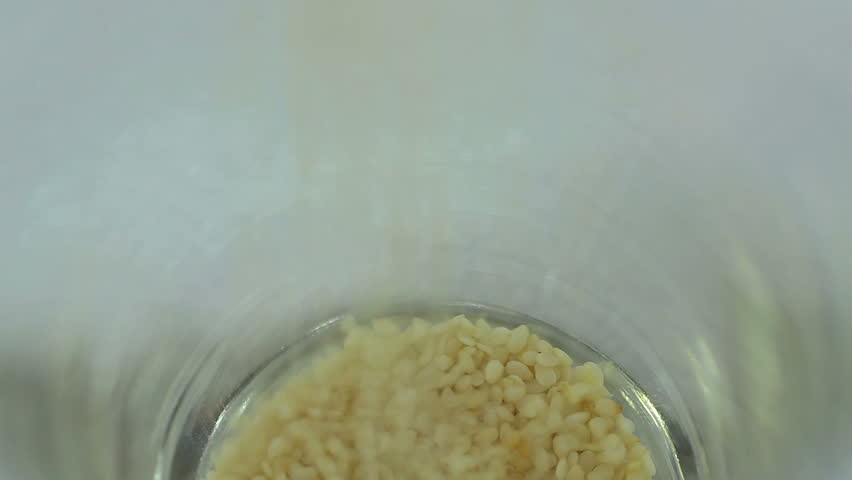 Pouring white sesame seeds into a glass.