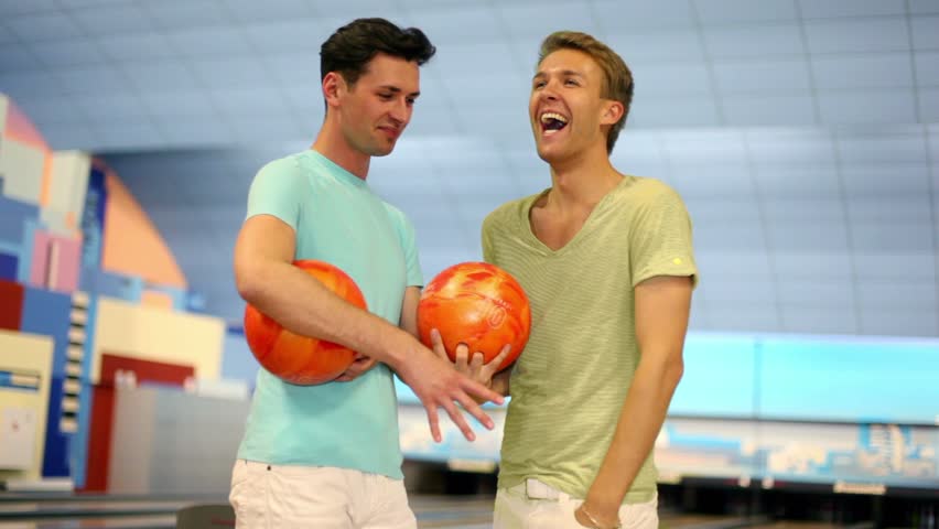 Two friends stand in bowling club with balls and talk