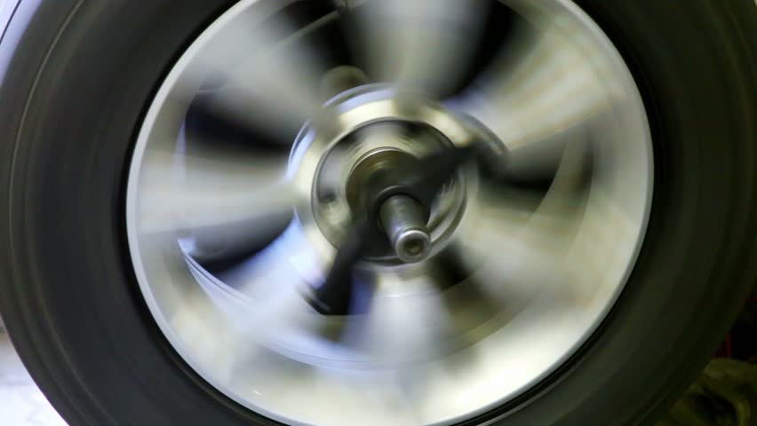 Car wheels spins on balance adjustment stand, man stops it and fixates
