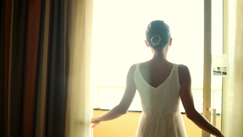 Woman stands near window and opens curtains in the morning