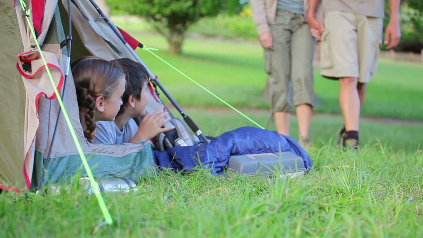 Smiling children waiting for their parents while lying in a tent in a parkland