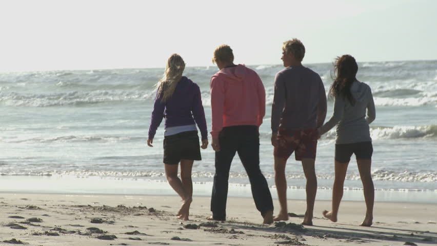 FOCUS SHIFT LONG SHOT PAN OF FRIENDS WALKING ALONG A BEACH