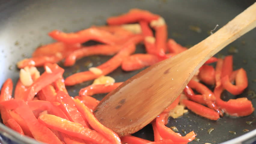 wooden spoon moving peppers over frying pan