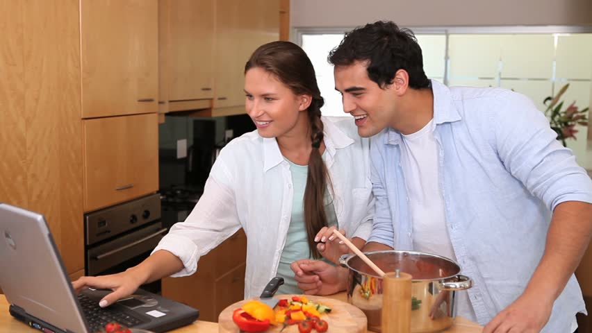 Laughing couple looking a recipe on a laptop in a kitchen