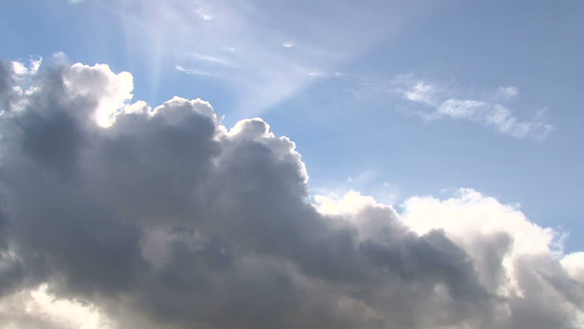 Beautiful cloudscape with large, building clouds and sunset behind shining sun rays and eventually breaking through cloud mass.