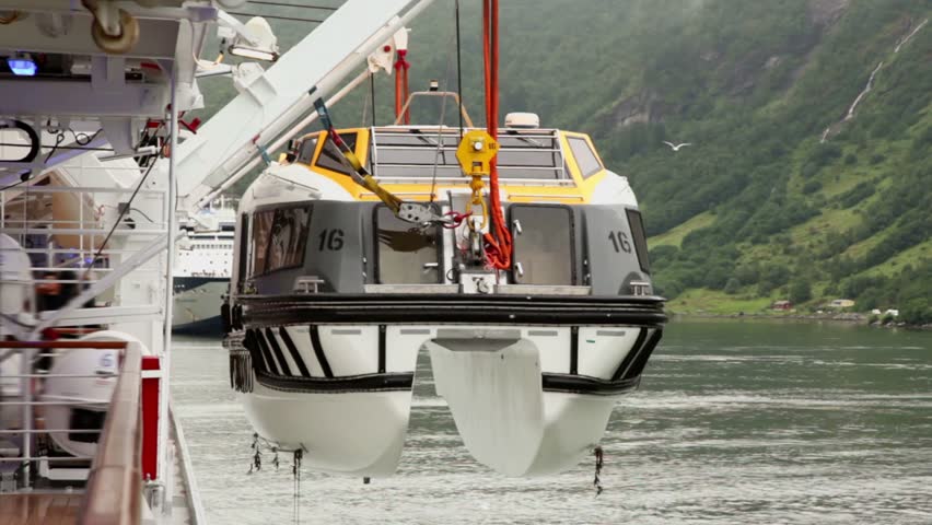 Crane lifts rescue boat to huge liner near of forest on mountain at shore