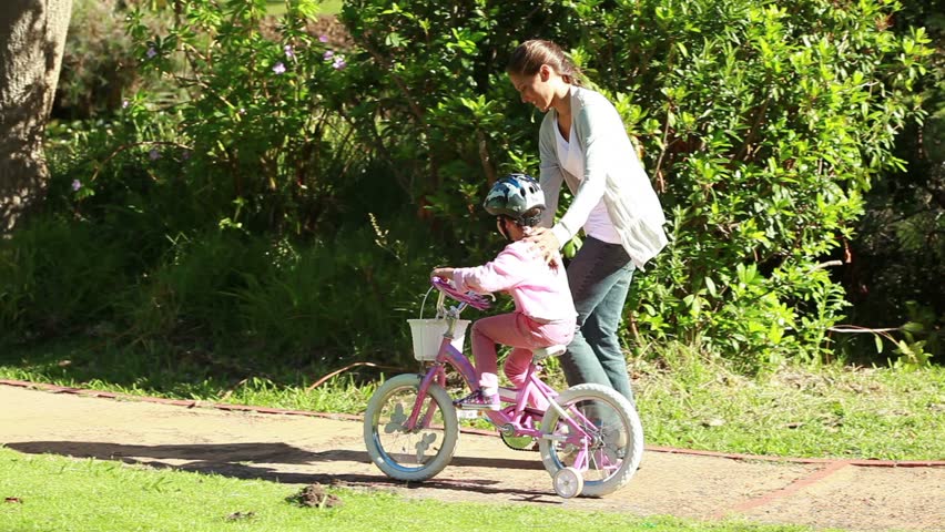 Smiling woman helping her daughter to ride a bike in a parkland