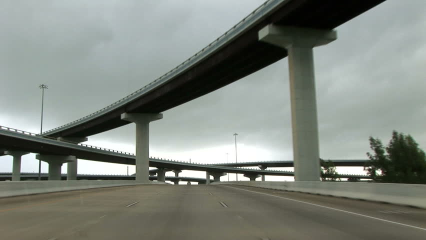 View from a moving vehicle of cloverleaf overpasses crisscrossing the highway. 