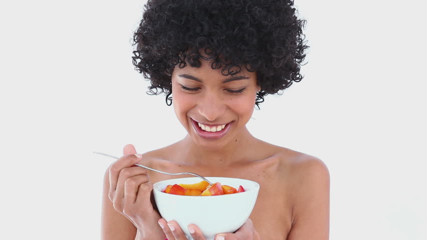 Smiling woman eating a fruit salad against white background
