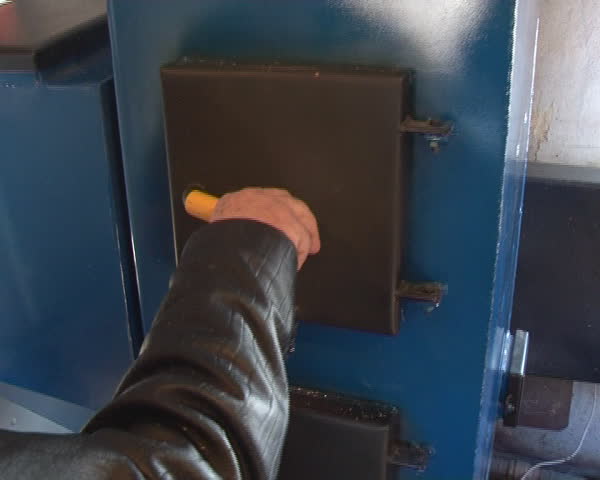 hand open boiler door. fire burning inside. boiler fired pellets and wood.