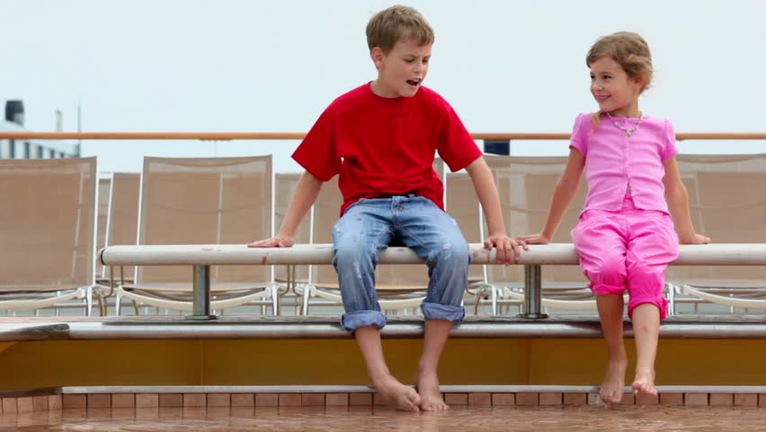Two kids boy and little girl sit at pool edge near deckchairs