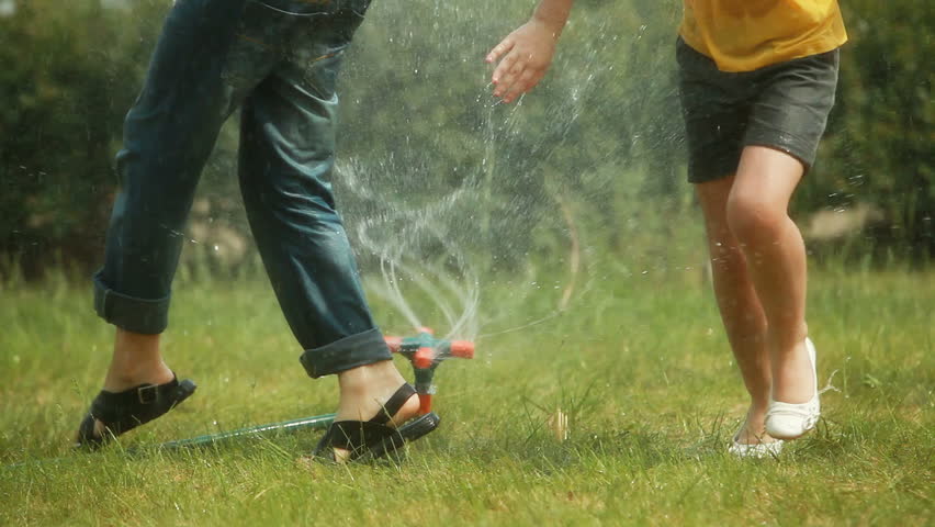 Carefree kids playing with sprinkler system trying not to get wet