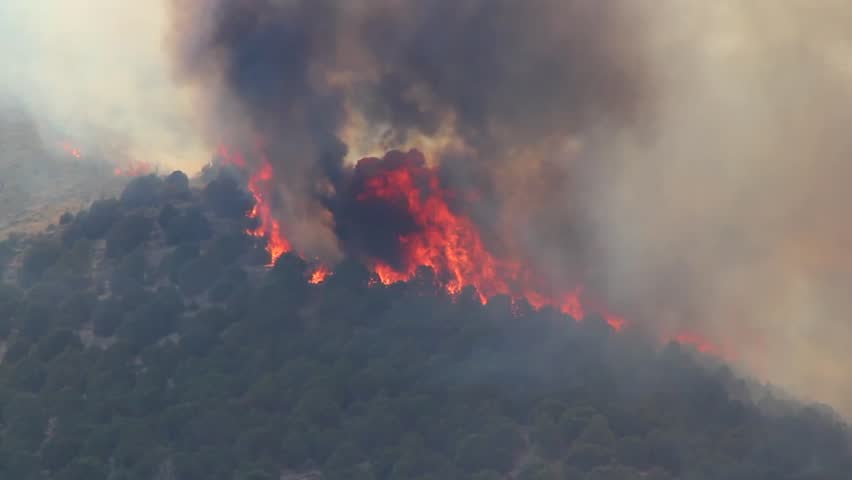 A raging wildfire burns across the mountain leaving a trail of smoke and ash.