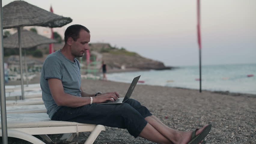 Young happy man with modern laptop on the beach
