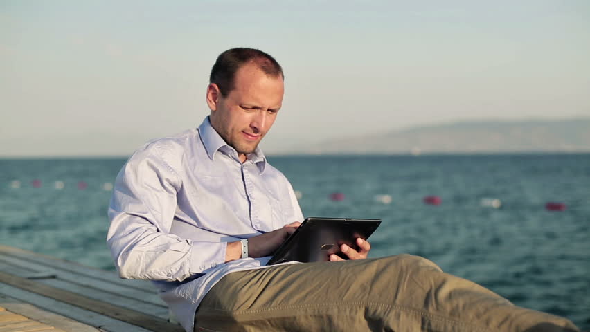 Happy man with tablet computer on wooden pier by the sea
